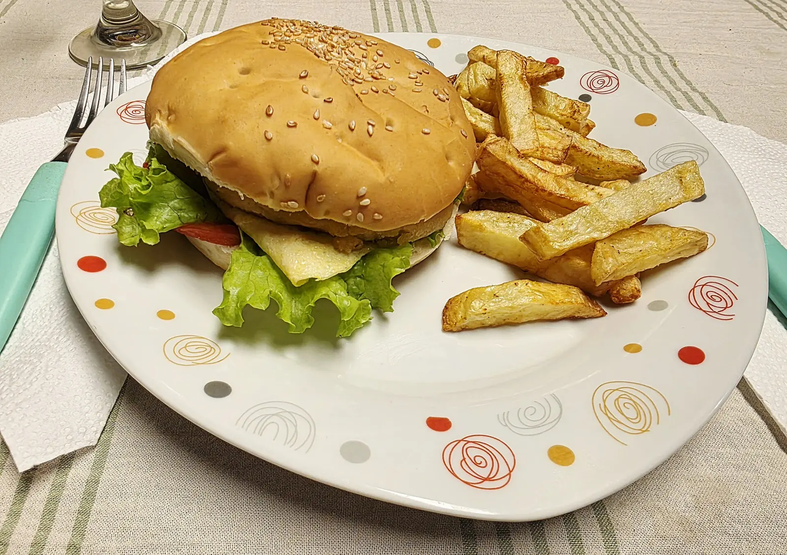 Homemade hamburger prepared in Argentina, served in a sesame-seed bun with lettuce, tomato and cheese, accompanied by rustic homemade French fries on a decorated plate.