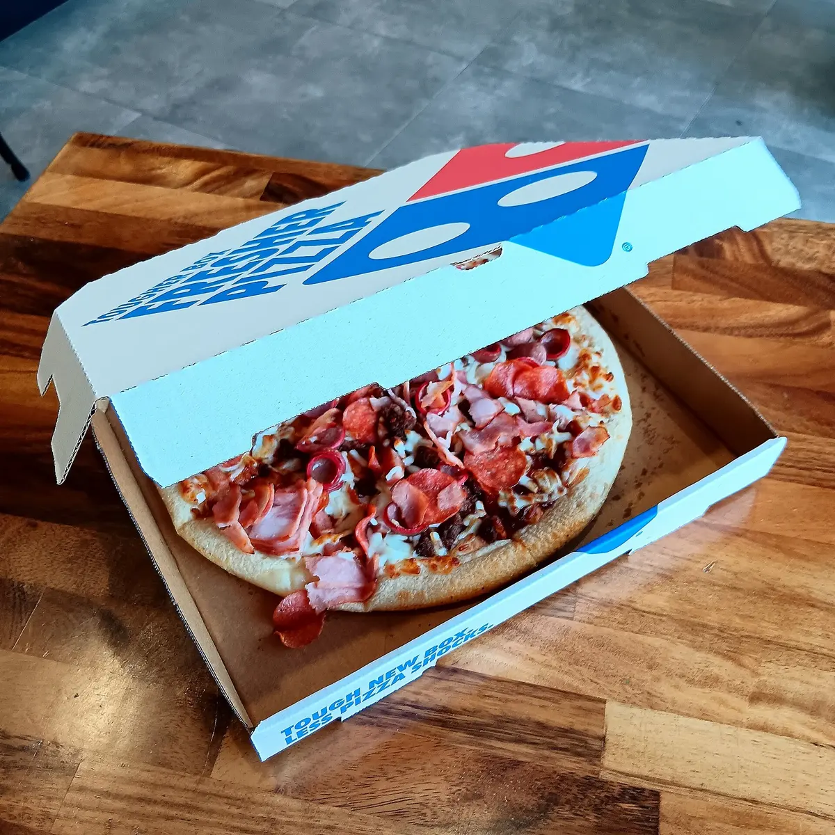 A BBQ Meatlovers Pizza, photographed in the dining area of Domino's Pizza Karawara – its toppings are described as 'Crispy bacon, pepperoni pieces, seasoned ground beef, smoked...