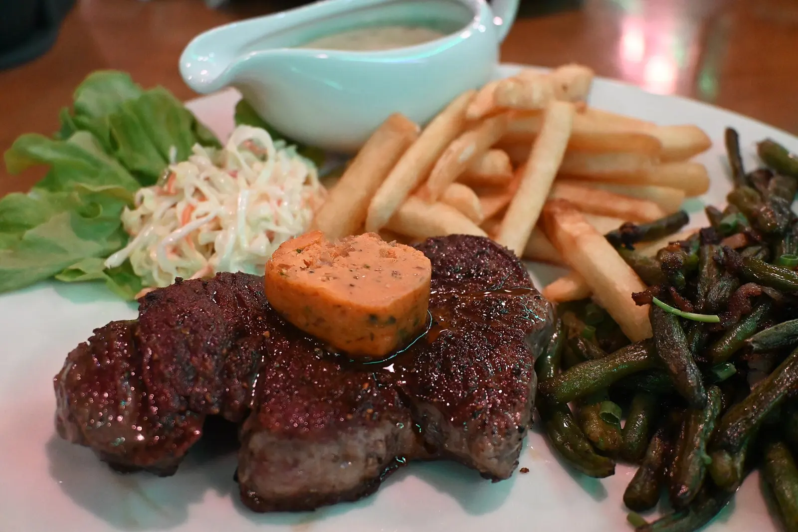 This photo shows a hearty meal served on a white plate. The main feature is a steak topped with what appears to be a pat of herb butter or flavored compound butter. Surrounding...