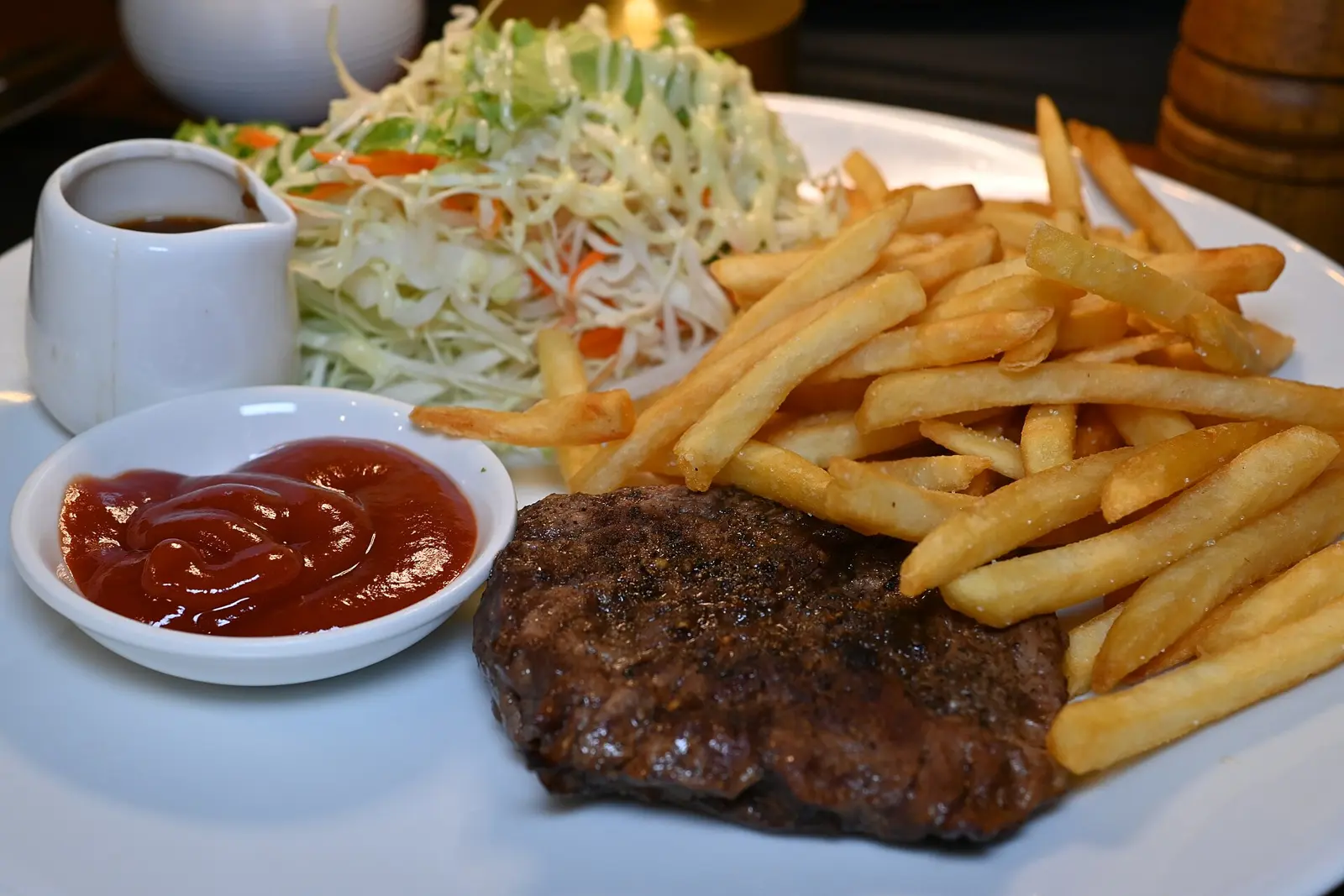 This photo shows a classic steak dinner plated on a white dish. The meal features a grilled beef steak as the centerpiece, accompanied by a generous portion of golden french...