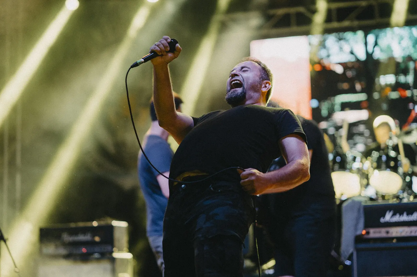 Musicians perform passionately on stage during an outdoor festival. The lead singer exudes energy while engaging with the crowd under colorful lighting.
