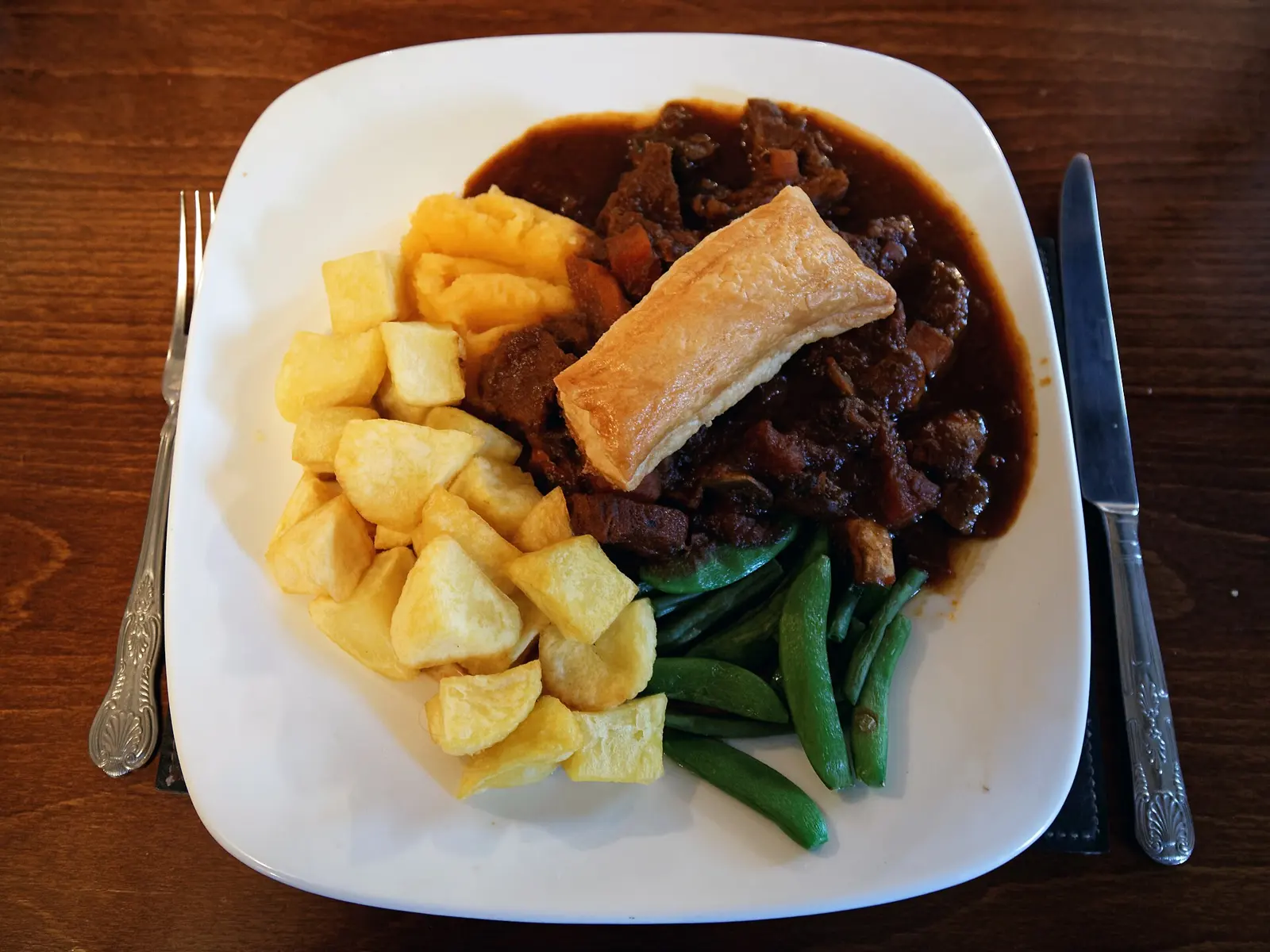 Main course of beef stew base topped with puff pastry , listed on the menu as a 'steak and ale pie', with sauteed potatoes and steamed sugar snap peas , at the White Hart Inn,...